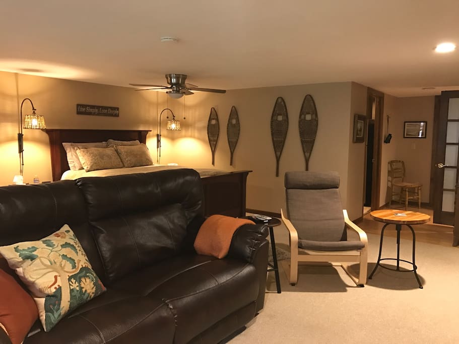 View of leather couch (w/2 recliners), bed, chair, hallway leading to walk-in closet, kitchen & bathroom.