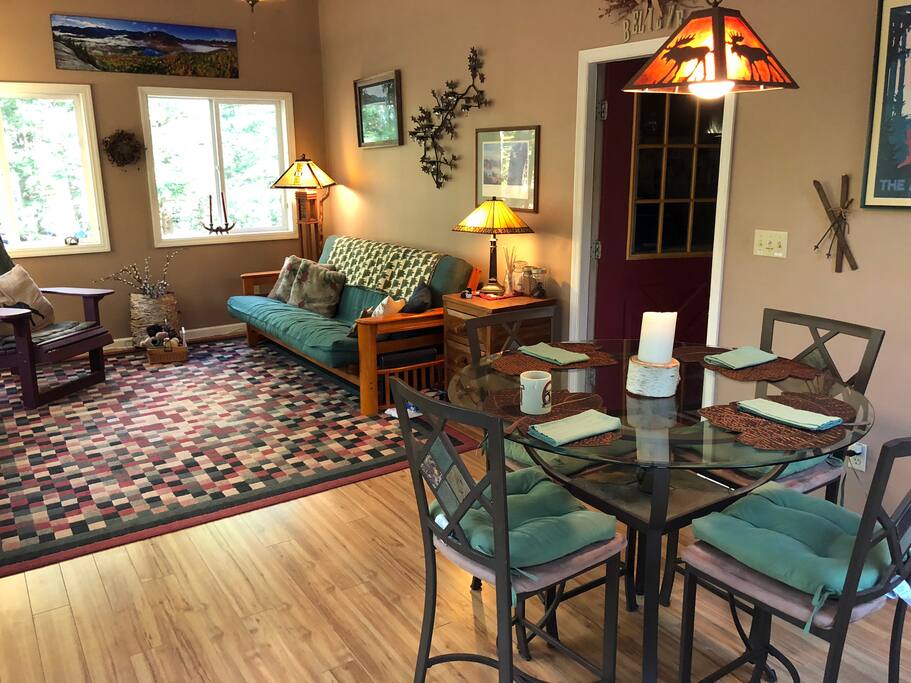 The Adirondack Room looking out to the back deck with BBQ grill. A high glass breakfast table with stool-height chairs is the perfect place for a meal or a card/board game and also serves as a beautiful place to sit and get some work done.