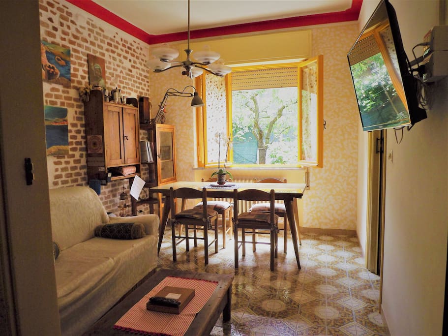 Sala da pranzo, televisore piatto, tavolo e dispensina, grande finestra che dà sul giardino privato.