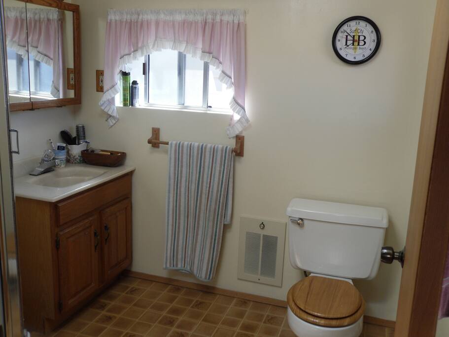 Upstairs bathroom with toilet, sink, shower, mirrors, window, heater, towel racks, fan & skylght.