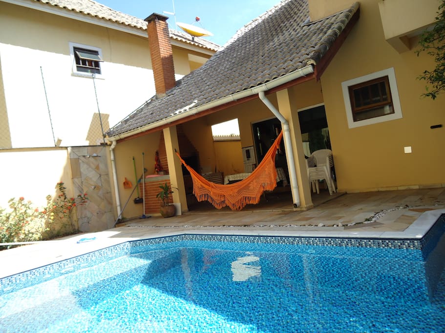 Os fundos da casa com uma piscina e churrasqueira com uma rede.
