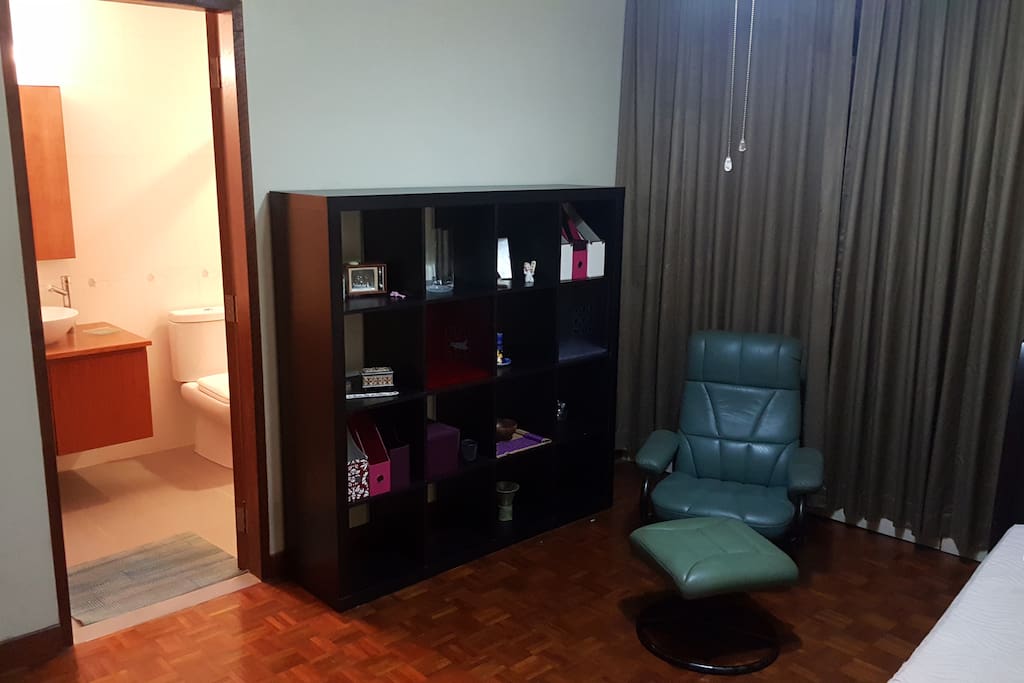 Large open shelving unit, entryway to the master bathroom and a comfortable reclining chair.