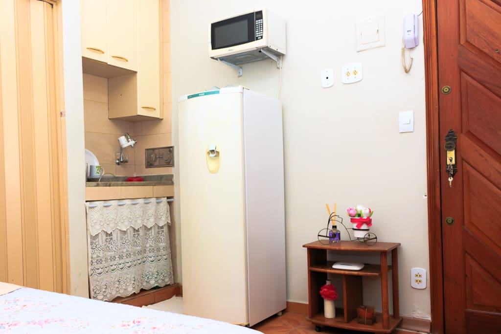 Cozinha com geladeira, microondas, liquidificador e utensílios (pratos, copos e talheres).