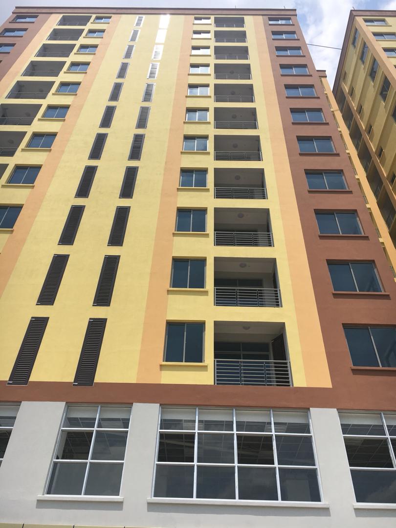 A tall multi-story building features a vibrant yellow and orange exterior. Large, modern windows are visible on each floor, allowing light to enhance the interior spaces. The ground level showcases expansive glass panels that provide a view of the area.