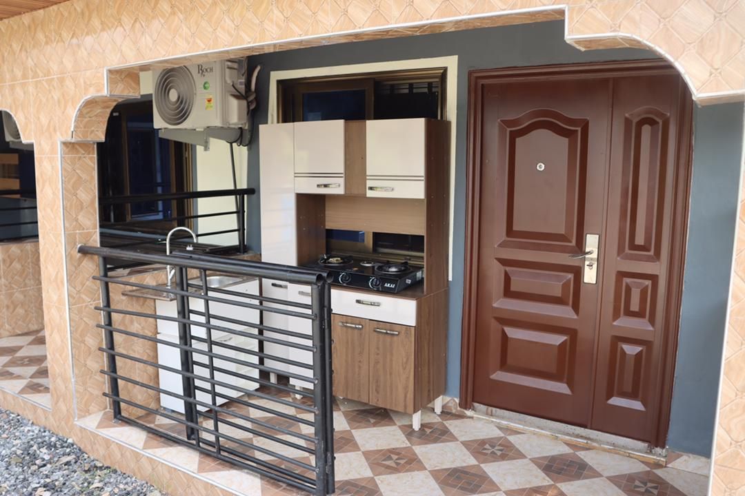 An outdoor kitchen area is featured, showcasing a compact design with modern appliances, including a gas stove and sink. A balcony with a metal railing provides access to the kitchen. A door with a polished finish leads to the interior space.