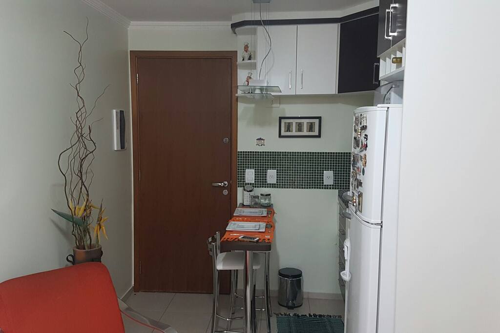 Área da cozinha com geladeira, micoondas, fogão e bancada para refeições