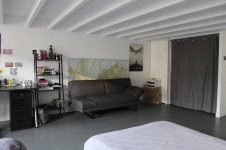 A spacious room is presented, featuring a comfortable sofa and a desk area. A map adorns the wall, providing visual interest. A light grey curtain separates the space, while the floor maintains a minimalist style with neutral tones.