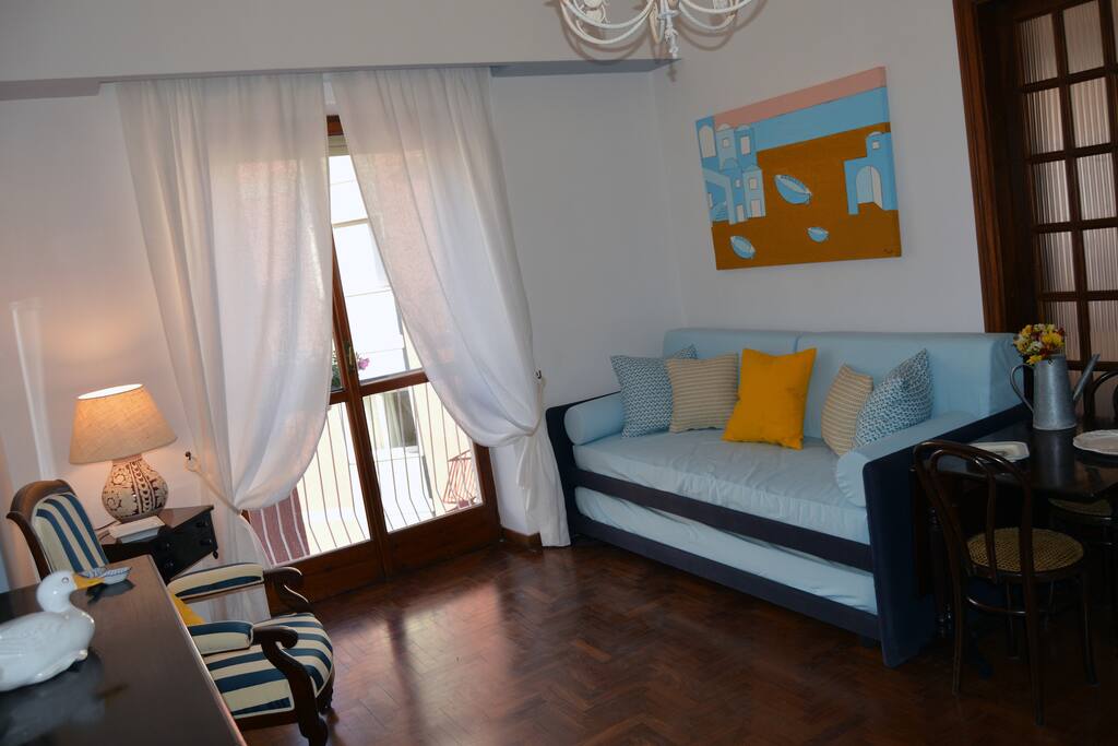 Salottino con angolo cottura. L'ambiente, corredato da divano letto (due posti letto), tavolo, poltrona e mobiletto buffet, è separato dalla camera da letto da un'antica porta scorrevole in mogano e cristallo.