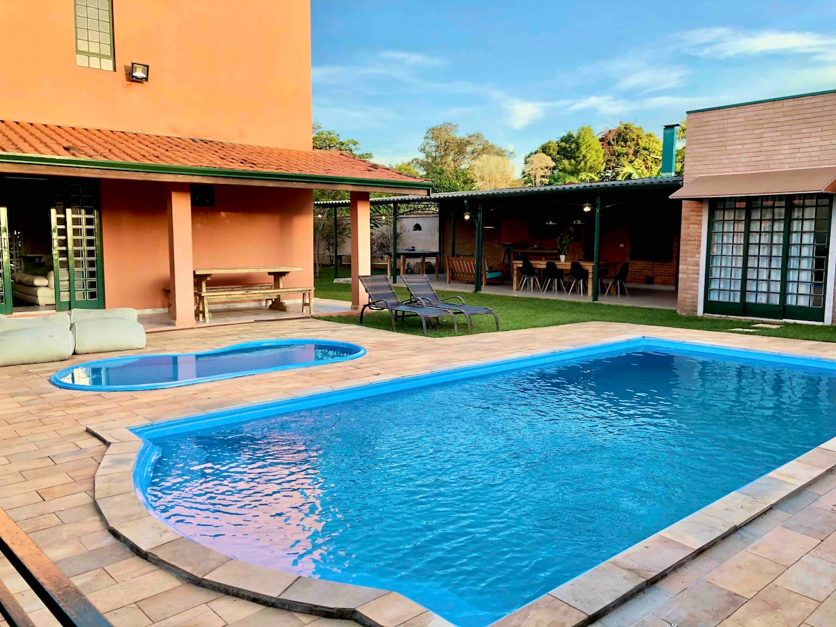 An inviting outdoor area is featured with two climatized swimming pools, one for adults and a smaller one for children. Comfortable lounge chairs are positioned around the pool, with a spacious covered area visible in the background, providing a relaxing setting for gatherings.