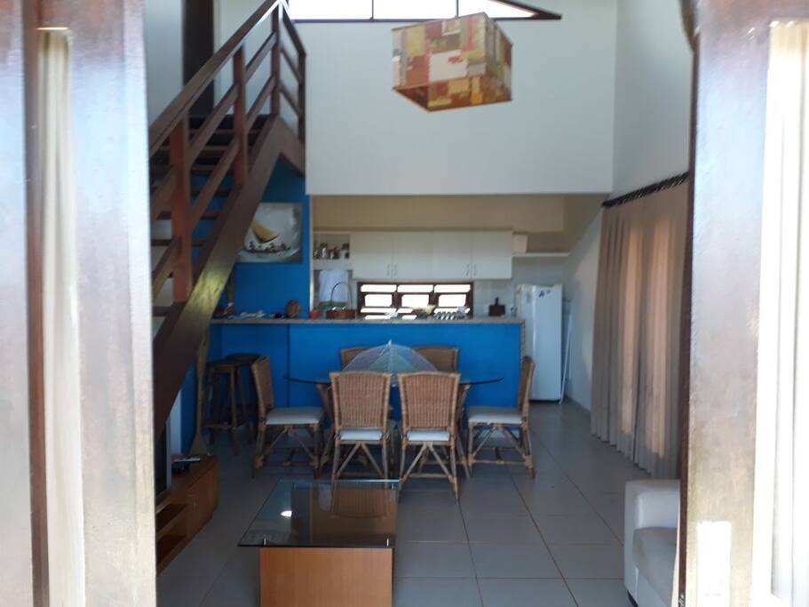 Vista sala e cozinha com geladeira, fogão, utensílios doméstico e escada com acesso ao solariumo.