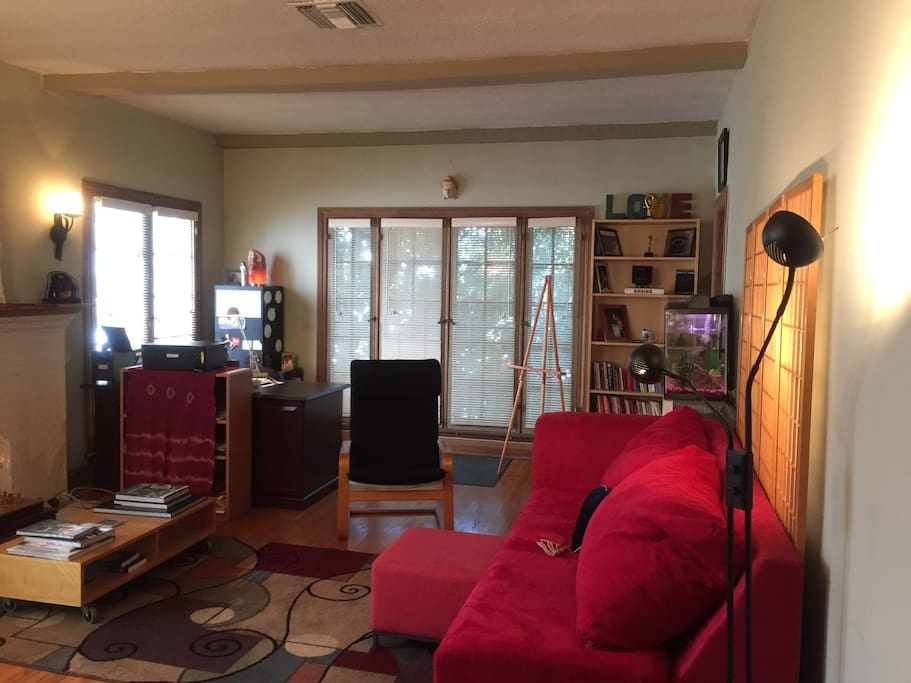 Large Living room with wooden floor high ceiling, French windows with wooden blinds plus full equipped office space with desk and fish tank.