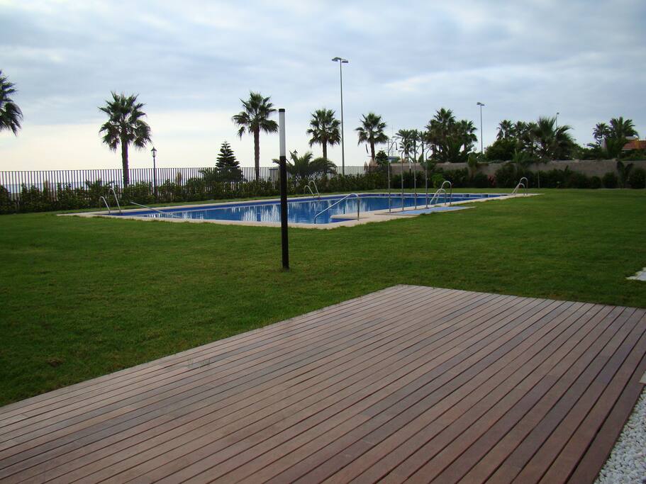 Vista del césped y la piscina con salida al paseo marítimo y a la playa directamente.