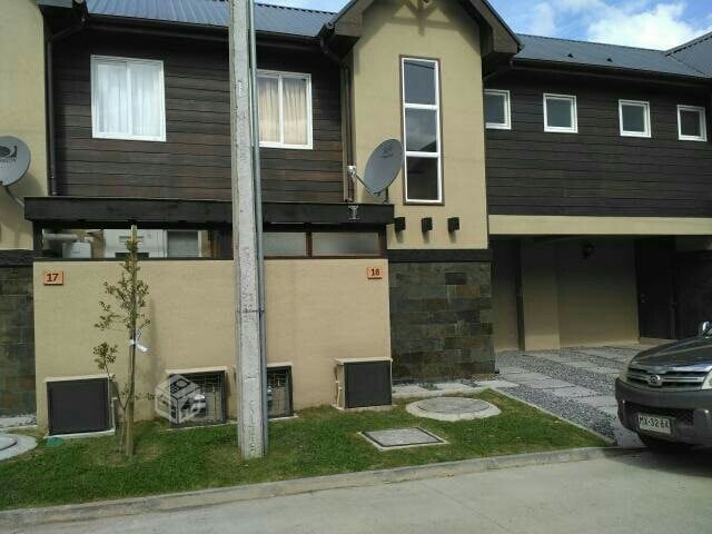 A two-story condominium is shown, featuring a combination of wooden and stucco facades. Ground-level air conditioning units are visible, along with a small landscaped area that includes grass and decorative stone pathways. The entrance is marked by numbers on the wall, ensuring easy identification.