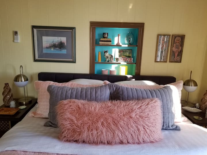 A close up of the pink/gray bed and shelf full of vintage lovelies and books for your reading pleasure.
