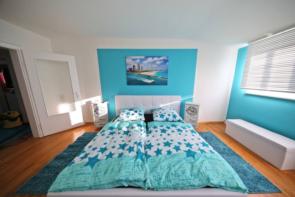 Schlafzimmer mit bequemen Doppelbett in wunderschönem Miami Türkis. TV ist ebenfalls im Schlafzimmer
