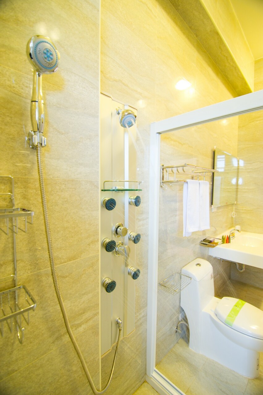 A modern bathroom features a glass-enclosed shower with multiple showerheads mounted on a smooth, tiled wall. Shelves hold toiletries, and fresh towels are neatly arranged. A sleek toilet is positioned adjacent to a stylish sink with a mirror above, contributing to a clean and functional space.