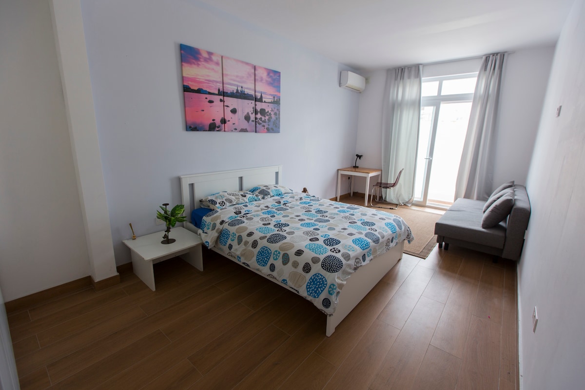 Spacious, silent, bright double bedroom suitable for 2-4 people with a sofa-bed, a wardrobe, fast WiFi, AC, balcony and a desk. The room comes with shared bathroom, kitchen and a yoga-fitness room where you are welcome to join one free yoga class. 