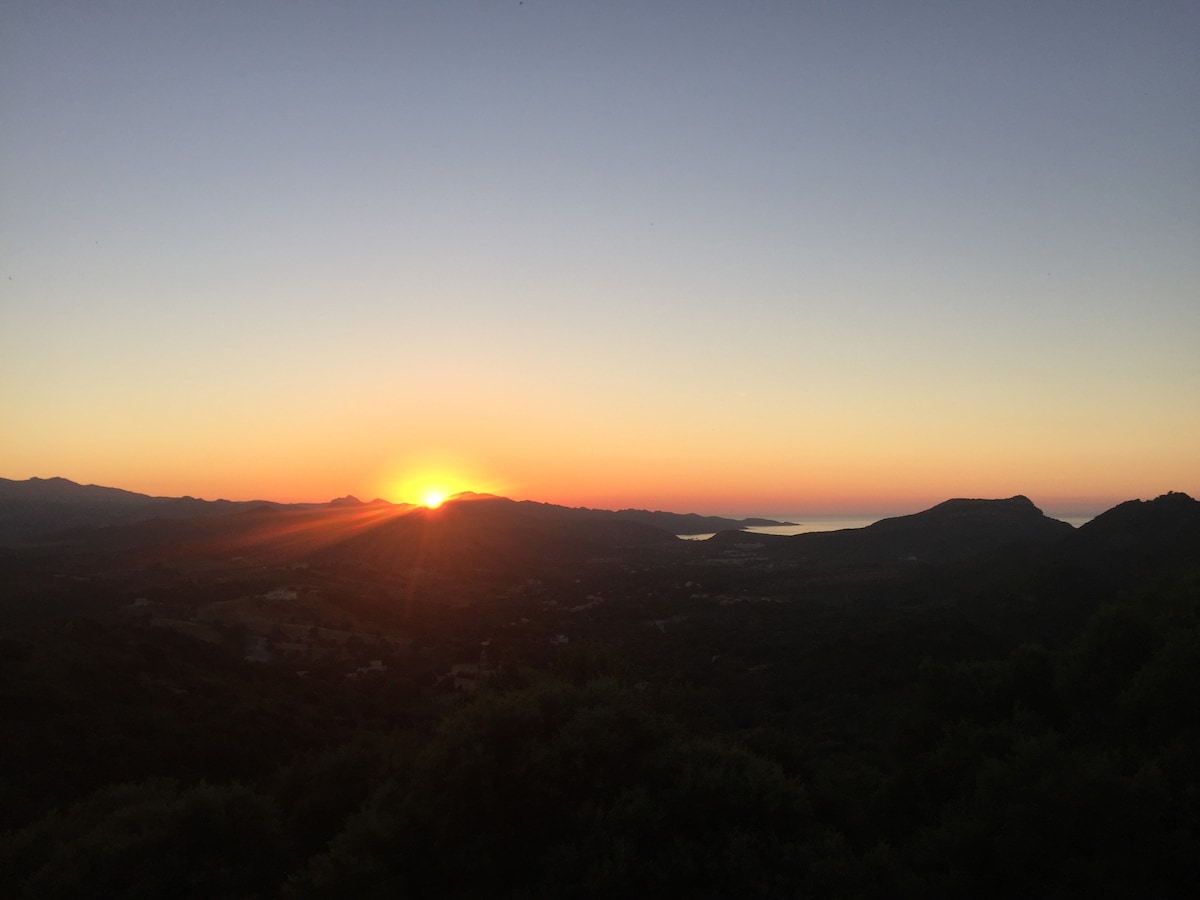 A scenic landscape captures the horizon as the sun rises, casting warm hues across the sky. The distant mountains and valleys are outlined against the vibrant colors, creating a tranquil view that invites contemplation.
