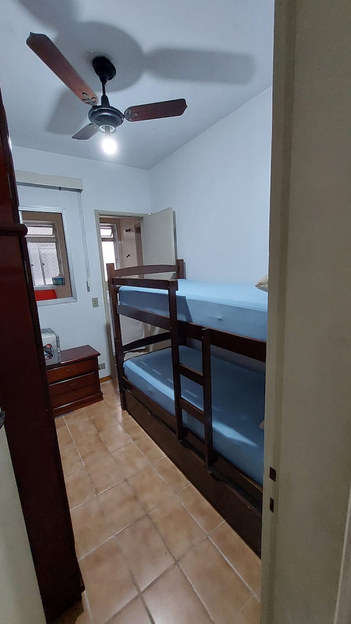 双面房间，配有吊扇、双层床和带保护套的床垫。