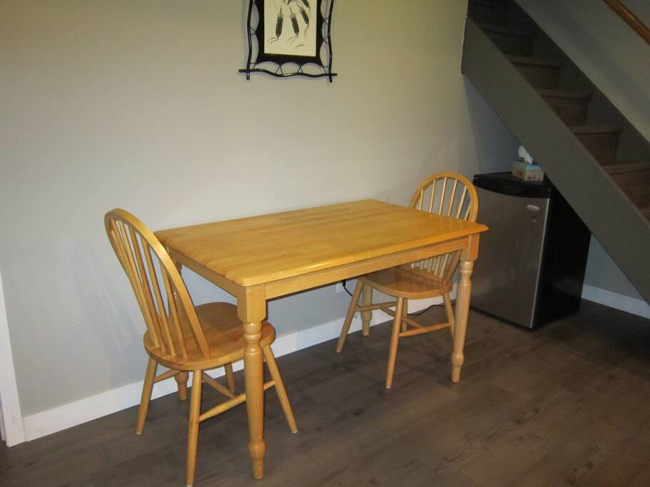 Extra table and chairs in basement with small fridge.