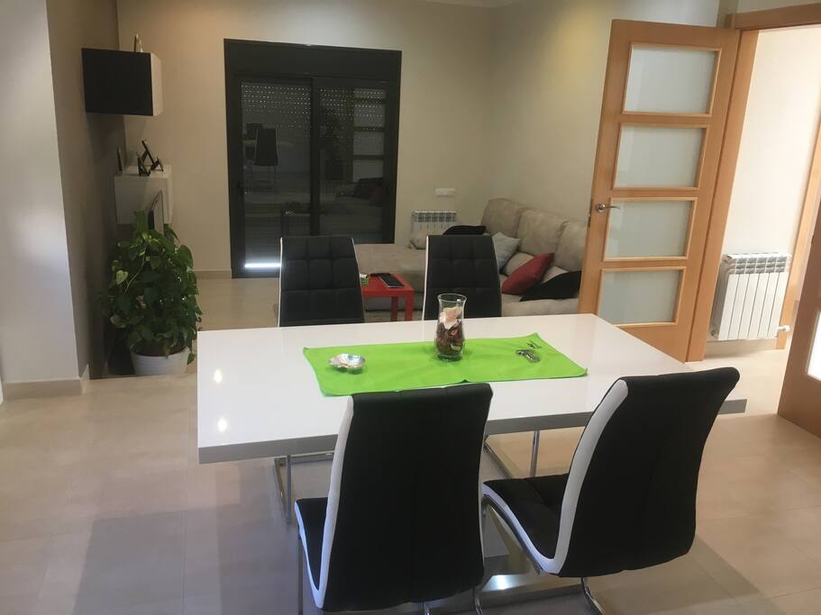 Salón/comedor con una mesa y cuatro sillas, donde caben hasta seis personas. Mucha iluminación.