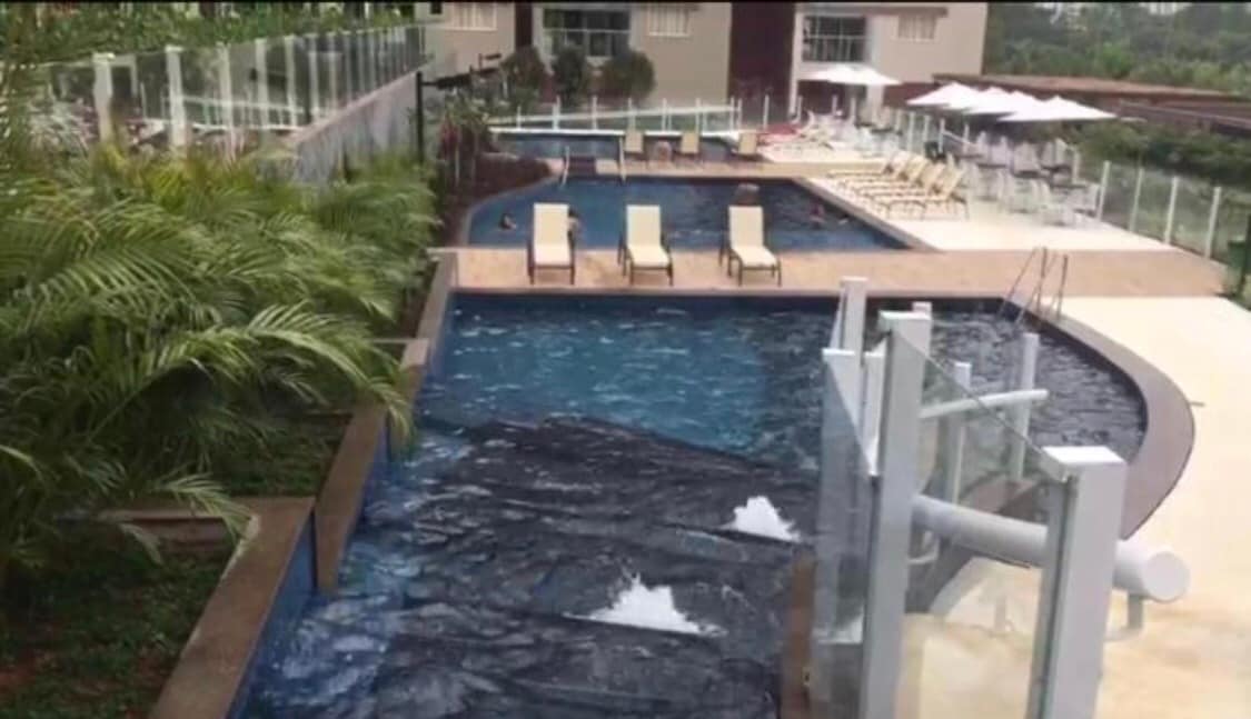 A resort-style pool area is showcased, featuring two distinct swimming pools. Sun loungers are arranged around the pools, and lush greenery provides a natural backdrop. Water features, including fountains, can be seen in the pool area, enhancing the overall ambiance.