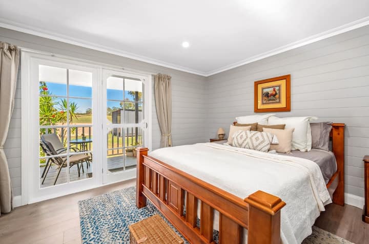 A spacious country bedroom with a comfortable queen bed, TV, futon, and overlooking a sunny veranda.