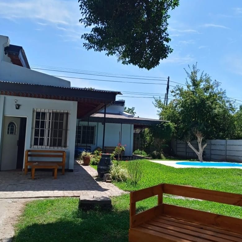 An outdoor area features a neatly maintained lawn, accompanied by a wooden bench and a stone pathway. A tranquil pool is visible in the background, surrounded by greenery with trees providing shade. The building showcases a combination of wood and stone finishes, enhancing the natural setting.