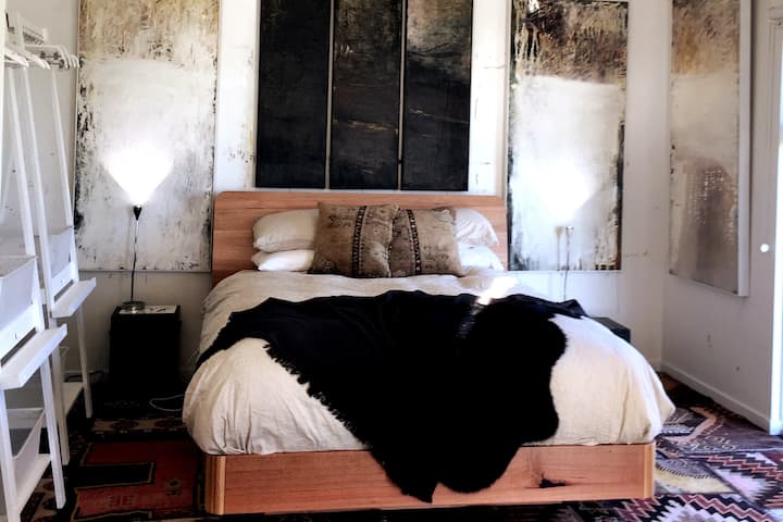 Tasmanian Oak bed made in Tasmania with extra plush mattress. Linen bedding. Artwork by Caroline Rannersberger, your host. Wardrobes are recycled easels. Mood lighting. We're going for a rustic romance vibe. Hope you feel it too.
