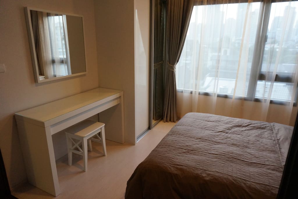 Comfortable bedroom with dressing table, wardrobe with hangers, new bed and bedding