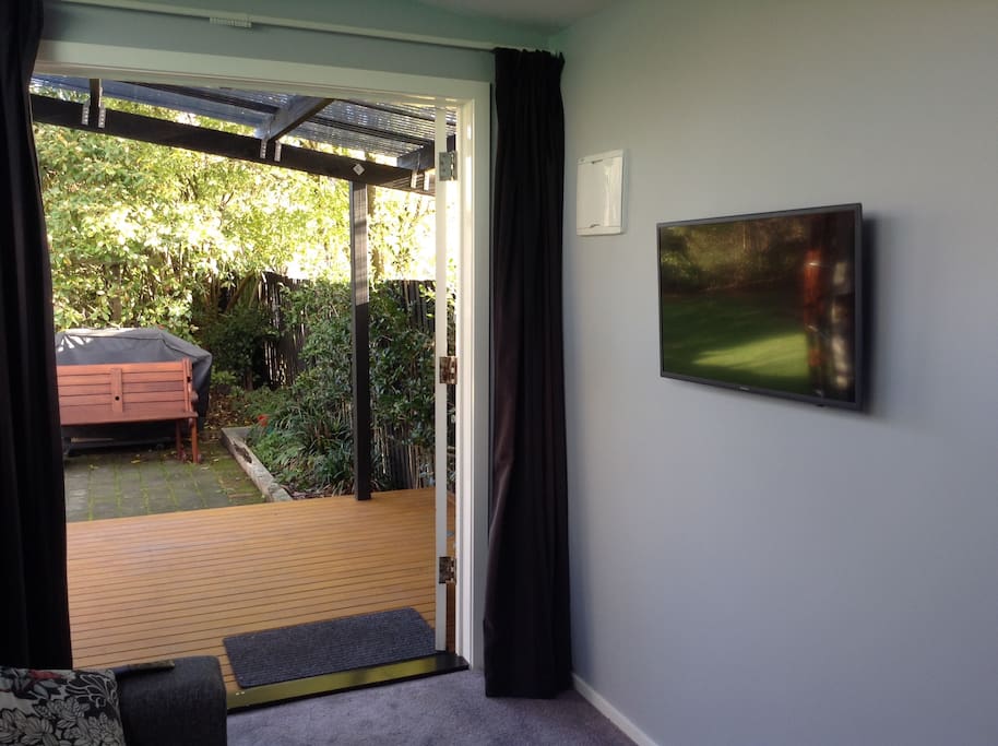 Interior of Sleepout by day looking out to garden showing deck and smart TV