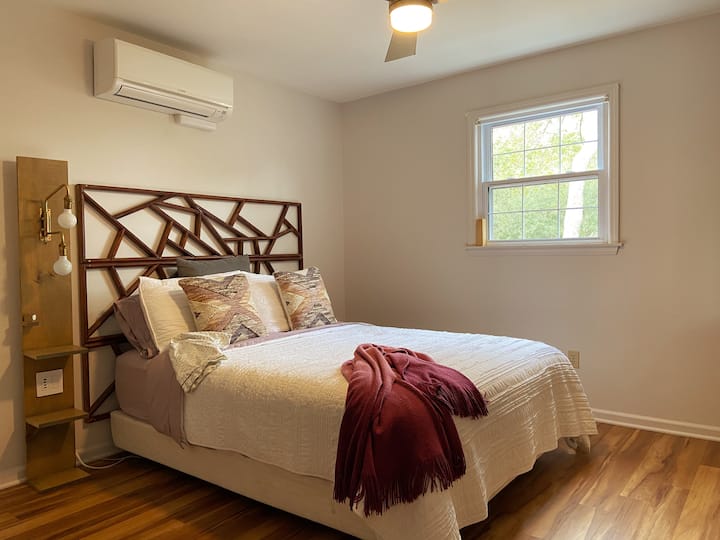 Spavaća soba s bračnim krevetom s noćnim ormarićem koji ima prigušiva svjetla i integrirane USB priključke za punjenje uređaja. Roletne (nisu na slici) za prozor pružaju gostima privatnost.