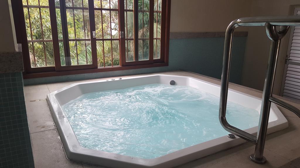 A spacious hot tub is positioned beside large windows, allowing natural light to illuminate the space. The bubbling water creates a serene ambiance, while the view of greenery outside enhances the relaxing atmosphere.
