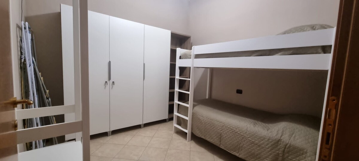 Eenpersoonskamer met stapelbed, kleerhangers en planken beschikbaar voor beddengoed.