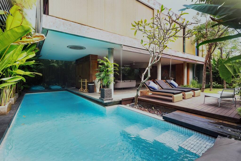 View from the large pool (half under cover and half in the sun). Looking towards the large lounge and dining area with stunning architectural spiral staircase.