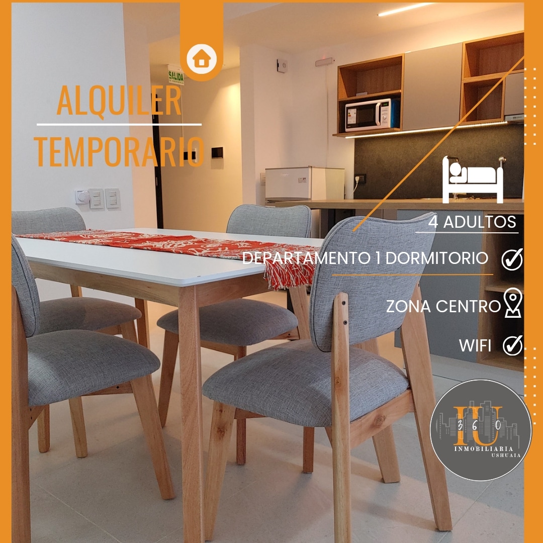 A modern dining area is shown, featuring a rectangular table with seating for four, surrounded by stylish gray chairs. An open kitchen area is visible in the background, equipped with contemporary appliances and finishes, enhancing the functional layout of the space.