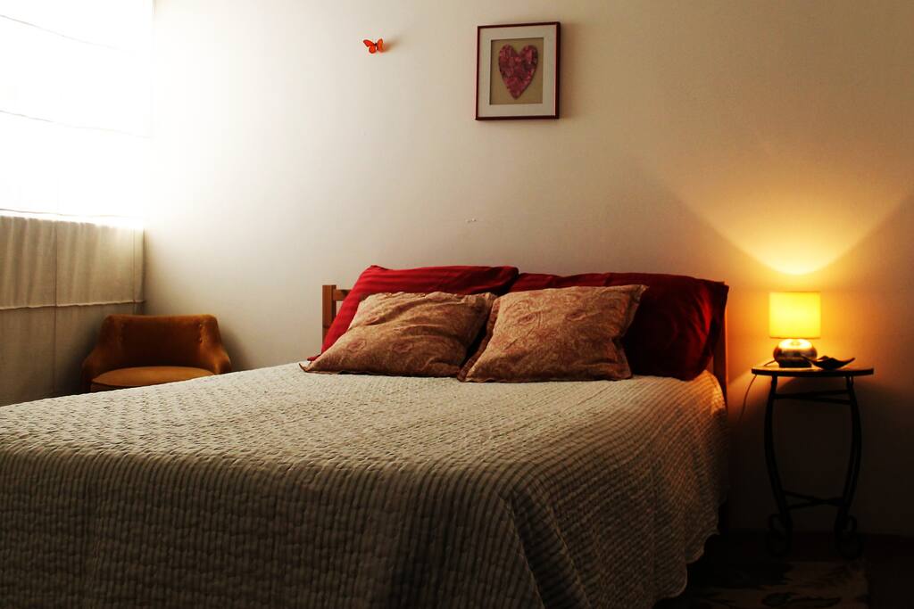 Habitación con cama matrimonial, cajonera, módulo para colgar ropa y lámpara de noche.