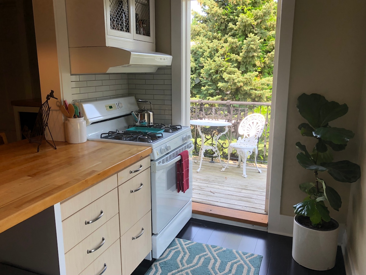 A well-appointed kitchen area features a wooden countertop, a white gas stove, and modern cabinetry. A sliding glass door opens to a balcony, where outdoor furniture is visible. A potted plant adds a touch of greenery to the interior space.