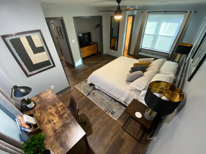 Пространата главна спална соба со брачен кревет, кадифена постелнина и многу перници ќе биде совршено место за одмор по долгиот ден.  Прозорците гледаат кон Кук Парк (проценет датум на завршување на почетокот на 2020 г.).  Прозорците се засенчени и има затемнети завеси во собата кои ќе ви помогнат да го добиете најдобриот можен сон.  Во плакарот има гардеробер и плакар за складирање и корпа за перење алишта.  Дали работите на ова патување?  Добре дојдовте во вашата канцеларија!  Има биро каде што може да го приклучите лаптопот за итна продуктивност пред прекрасен прозорец и светло за задачи.