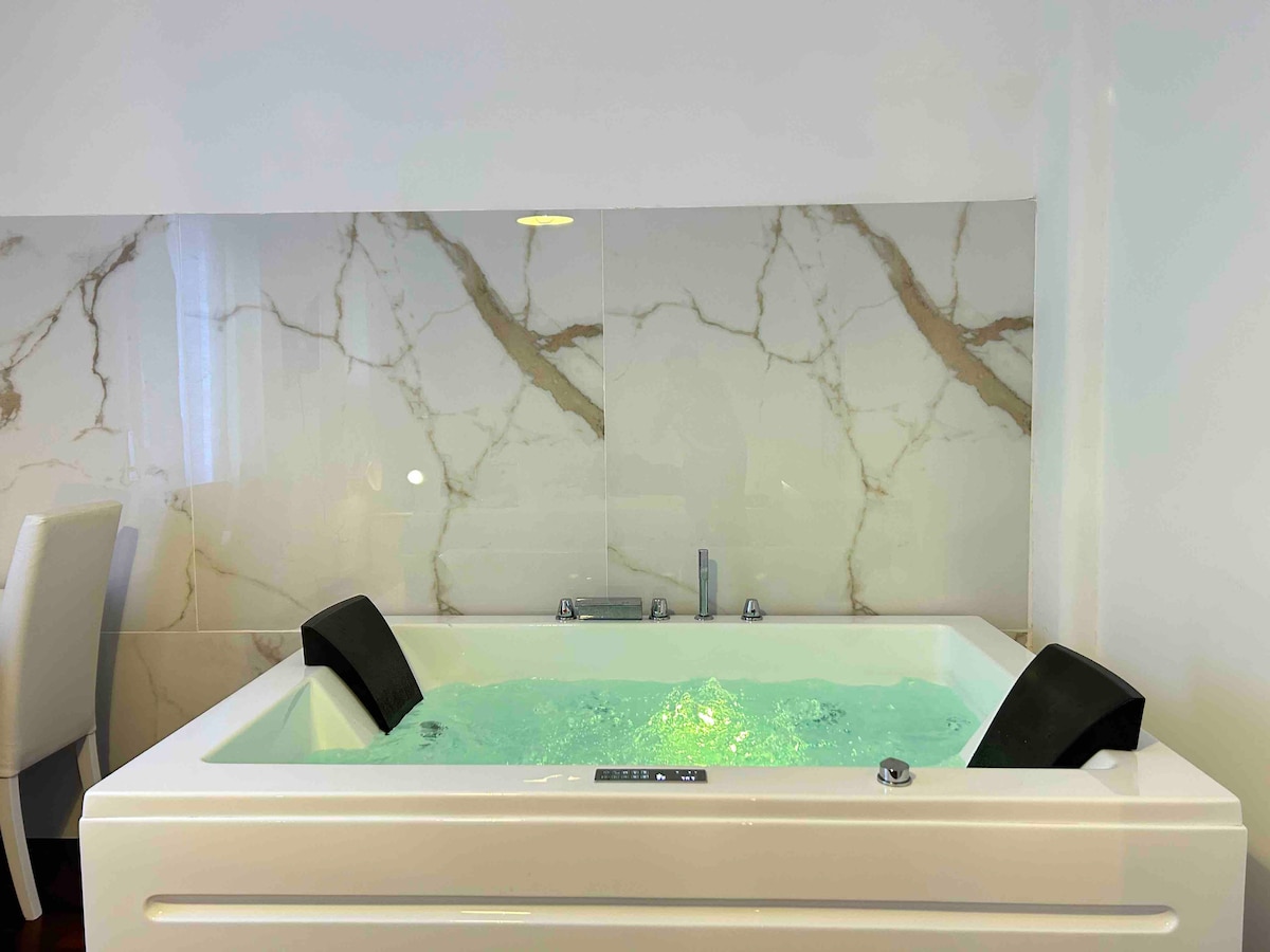 A modern jacuzzi is surrounded by elegant marble wall finishes. Soft green water is visible, along with sleek black jets on either side. The space is well-lit, enhancing the serene atmosphere.