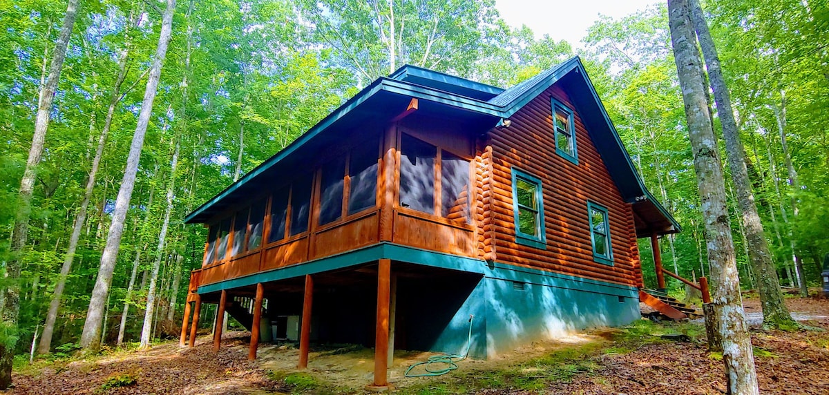 The log cabin retreat is surrounded by lush greenery, with a spacious screened-in back porch that provides a seamless connection to the outdoors. Wooded trails can be accessed directly from the property, offering a serene escape in nature.
