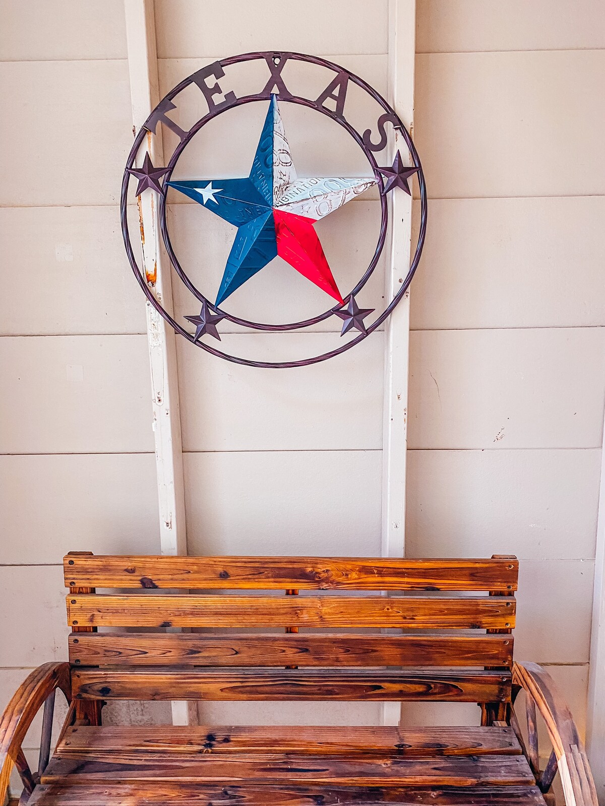 A rustic wooden bench is positioned against a light-colored wall, featuring a decorative Texas star emblem in red, white, and blue. The star is set within a circular metal frame, adding a regional touch to the inviting space.