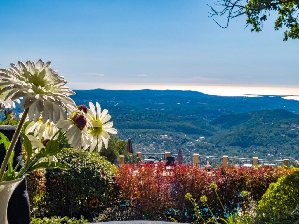 A vase of white flowers is positioned in the foreground, with a panoramic view of the lush, rolling hills and the coastline visible in the background. The scene is bright, with clear blue skies and the subtle shimmer of the sea in the distance.