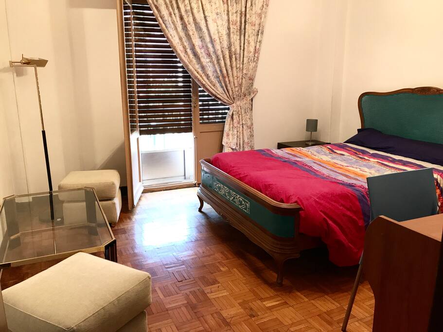 Habitación con balcón, cama doble, escritorio, armario grande y mesita con pufs.
