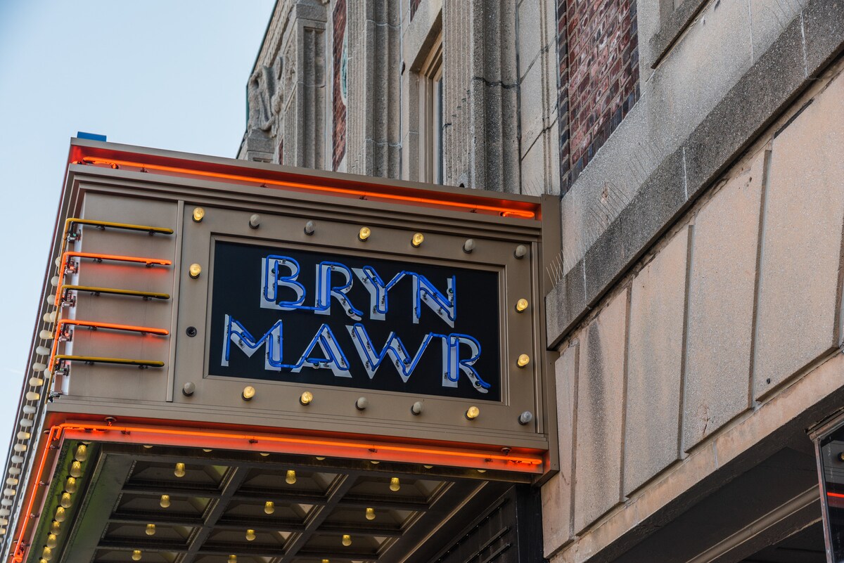 The marquee sign for the Bryn Mawr Theater is prominently displayed, featuring bold blue letters against a golden background. Surrounding lights accentuate the theater's name, creating a distinctive look that stands out against the historical brick facade.