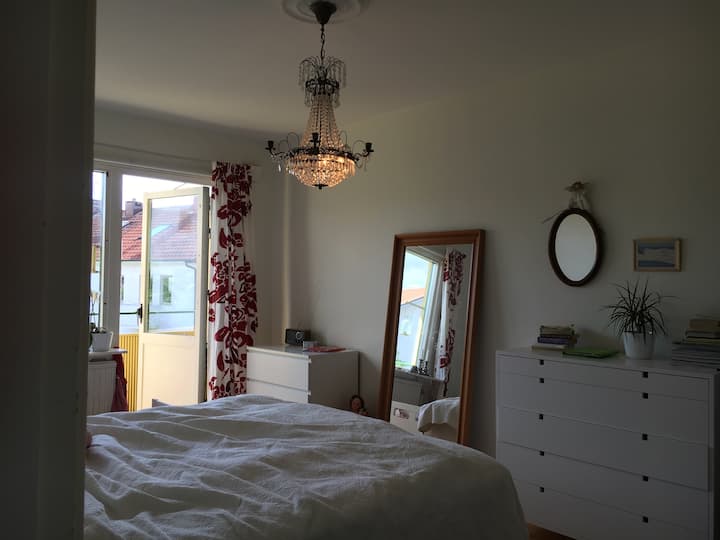 Quarto com cama de casal e cama de bebê ao lado. Varanda com sol noturno.