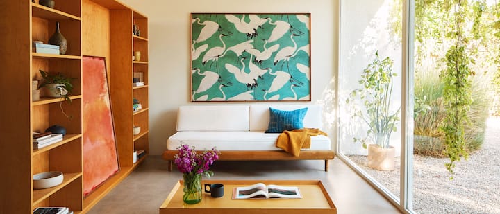 Una foto ritrae una stanza luminosa e ariosa decorata con due grandi dipinti: uno appeso sopra al divano e uno sistemato all'interno di uno scaffale disposto contro la parete.