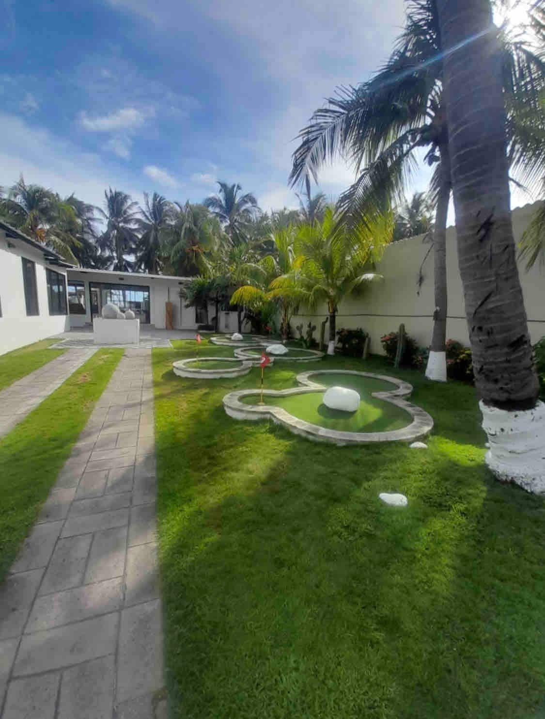 A well-maintained garden features a manicured lawn with stone pathways and decorative flower-shaped elements. Lush palm trees provide shade, and bright tropical foliage enhances the outdoor space. The setting offers a blend of greenery and stone, inviting relaxation and outdoor enjoyment.