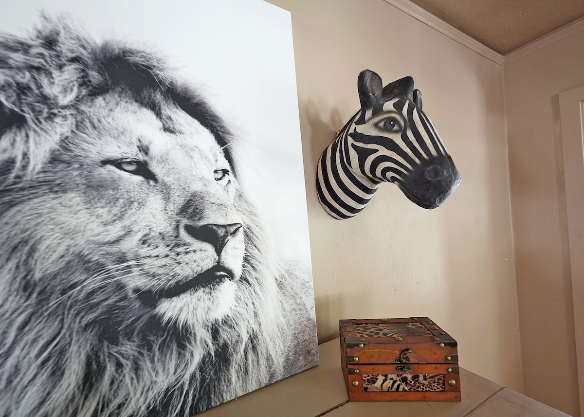 A decorative zebra head mounted on the wall is complemented by a large, abstract black and white artwork nearby. A stack of vintage boxes with animal print designs rests on a surface below. The overall arrangement adds a unique touch to the interior decor.