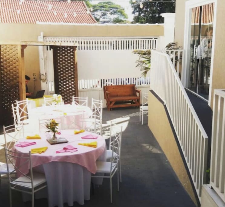 Nossa área de lazer/convívio - com bancos de madeira, pergolado, pufes, mesas e cadeiras. Onde servimos o café da manhã.